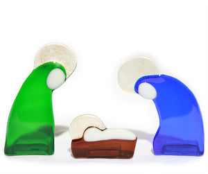3 stylized pieces made from coloured glass representing the holy family, Mary, Joseph and baby Jesus in a manger